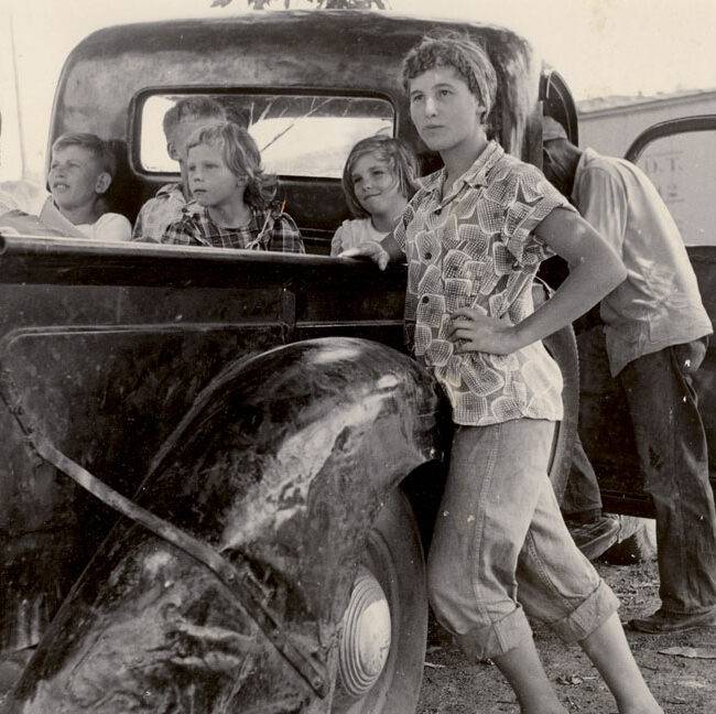 Black and white historical image of a migrant family standing next to truck at Flamm Orchards in Cobden, IL.